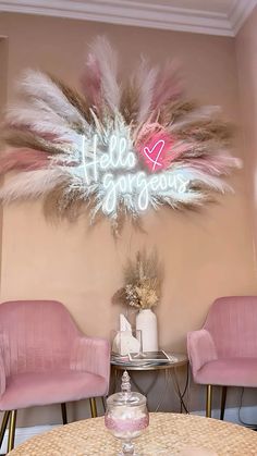 two pink chairs sitting in front of a table with a neon sign above it that says hello gorgeous