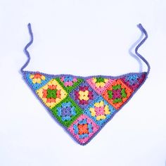 a multicolored crocheted triangle is hanging from a string on a white background