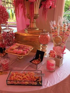 a table topped with lots of candy and candies next to a tall vase filled with pink flowers