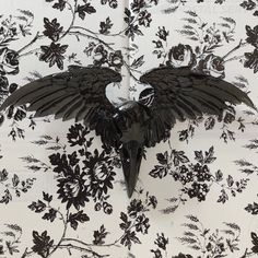 a black bird with wings spread out on a white floral print wallpapered background