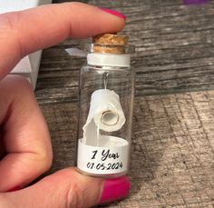 a hand holding a tiny glass bottle with a roll of toilet paper in it that says 1 year