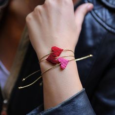 a woman wearing a red and pink bracelet with two hearts on it's wrist