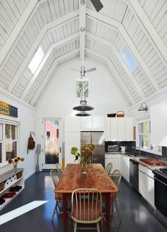 a kitchen with a wooden table surrounded by white cabinets and appliances, along with an open floor plan