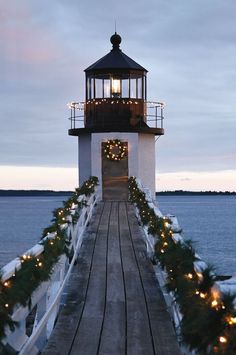 a light house is lit up with christmas lights and garlands on the walkway leading to the water