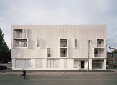 a person riding a bike past a tall white building