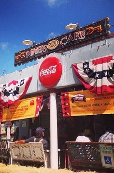 people sitting at tables in front of a restaurant with banners on the side of it