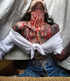 a woman with tattoos on her body and chest sitting in front of a white curtain