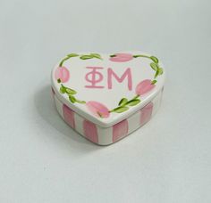 a pink and white heart shaped box with the letter m on it's lid