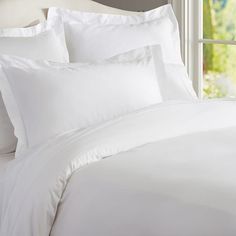 a bed with white sheets and pillows next to a window