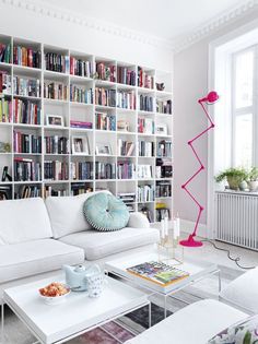 a living room filled with lots of white furniture and bookshelves full of books