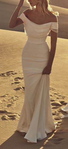 two women standing in the sand with their hands on their hipss, one wearing a white dress