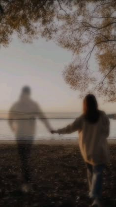 two people holding hands and walking on the beach at sunset or dawn with blurry trees in the foreground