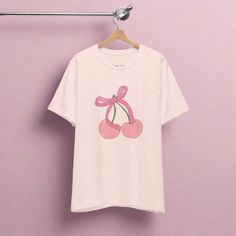 Embrace the sweetness of the current coquette trend with this adorable design featuring two plump pink cherries adorned with a cute, pink bow. Perfect for adding a playful touch to your wardrobe, this t-shirt combines whimsy with style, making it an ideal choice for any fashion-forward individual. Whether you're strolling through the city streets or enjoying a casual outing with friends, the "Cherry Bowby" tee is sure to turn heads and spark conversations. Indulge in the irresistible allure of o Summer Pink T-shirt With Cute Design, Casual Pink T-shirt With Cute Design, Pink Casual T-shirt With Cute Design, Pink Cute Crew Neck T-shirt, Cute Pink Crew Neck T-shirt, Trendy Pink Tops With Cherry Print, Cute Pink Fruit Print Tops, Cute Bow T-shirt For Spring, Cute T-shirt With Bow For Spring