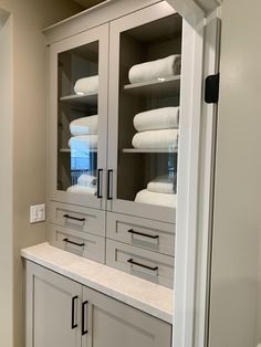 a cabinet with glass doors and white towels on it's shelves in a bathroom