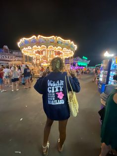 a woman standing in front of a carousel at night with her back to the camera