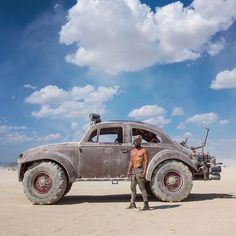 a man standing next to an old car in the desert