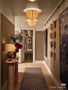 a hallway with two lamps and paintings on the wall next to a lamp shade that is hanging from the ceiling