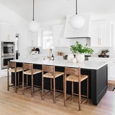 a kitchen with white cabinets, black island and wooden stools in front of an oven