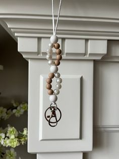 a wooden beaded necklace hanging from a hook on a white cabinet door with flowers in the background