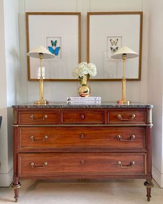 a dresser with two lamps on top of it next to a painting and flowers in vases