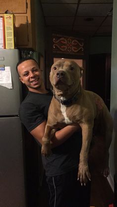 a man holding a dog in his arms while standing next to a refrigerator freezer