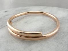 "This can easily be worn alone, but would look great stacked with other bracelets as well. The bangle is round, crafted of a solid, 5.5mm wide rose gold, slightly domed on top and doubled over itself to create a bypass. This is such a simple design, and so pretty on the wrist! Metal: 9Ct Rose Gold Width: 11.6 mm (at widest point) Inside Diameter: 3 Inches Marks: \"9Ct 9Ct\" Stamped on the inside SKU #: Q0JV36-P Each piece has been identified and graded by a Graduate Gemologist who has been certi Eternity Bands, Gold Jewellery, Bangle Bracelet, Simple Design, So Pretty, Simple Designs, Bangle Bracelets, Gold Jewelry, Gold Bracelet