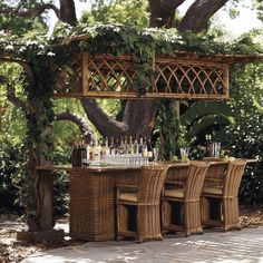 an outdoor bar set up with wicker chairs and bottles on the table, surrounded by greenery