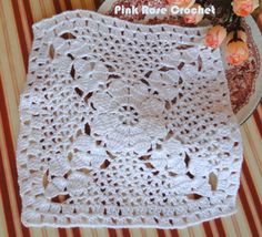 a white crocheted doily sitting on top of a table next to a vase filled with flowers