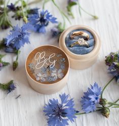 two wedding rings sitting in a box next to blue flowers