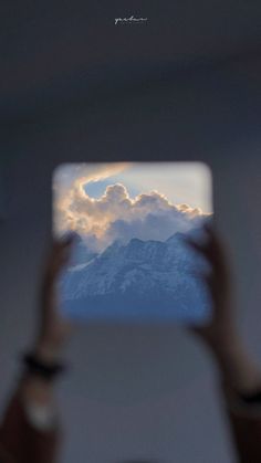 a person holding up their cell phone to take a photo with the sky and mountains in the background