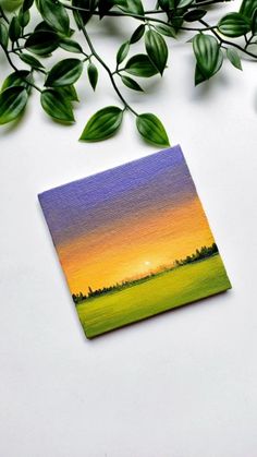 a card with an image of a sunset in the distance and green leaves surrounding it