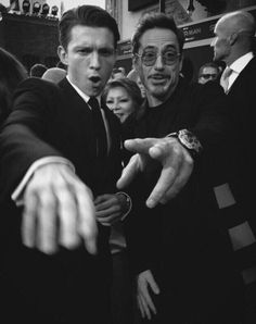 black and white photograph of two men pointing at each other with people in the background