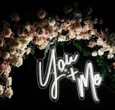 a neon sign that reads you and me surrounded by flowers on a black background with the words you and me spelled in white letters