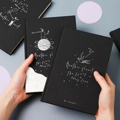 two black notebooks with drawings on them being held up by someone's hands