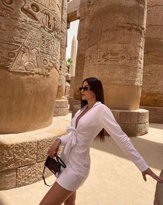 a woman standing in front of an egyptian temple wearing sunglasses and a white shirt dress