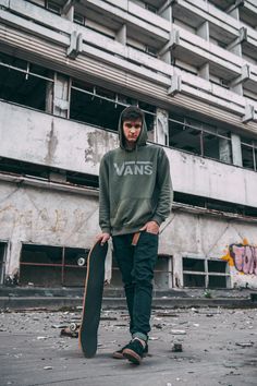 a young man holding a skateboard in front of an abandoned building