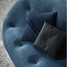 two black pillows sitting on top of a blue round couch next to a pillow case