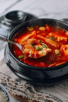 a bowl of soup with meat and vegetables in it on a wooden table next to rice