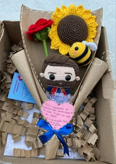 an open box with two stuffed animals and flowers in it, on top of cardboard