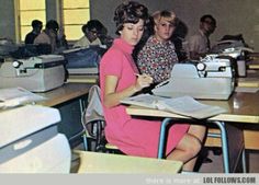 two women are sitting at desks in an old fashioned classroom, one is typing on a typewriter