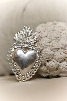 a silver heart shaped brooch sitting on top of a white couch next to a pillow