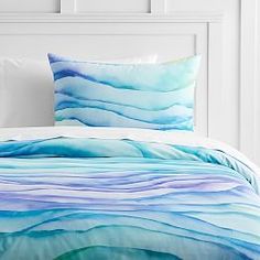 a bed covered in blue and white sheets with waves on it's pillow cases