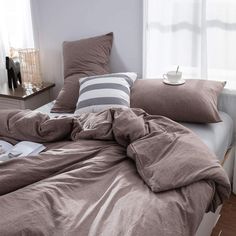 an unmade bed with two pillows and a blanket on it in a bedroom next to a window