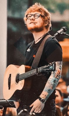 a man holding a guitar while standing in front of a microphone and people behind him