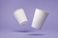 two white coffee cups are flying in the air on a purple and blue background, one is upside down