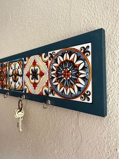 a wall hanging with several colorful tiles and keys on it's hooks in front of a white wall