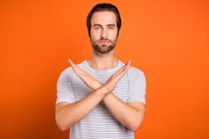 a man with his hands folded up in front of an orange background is making a stop sign