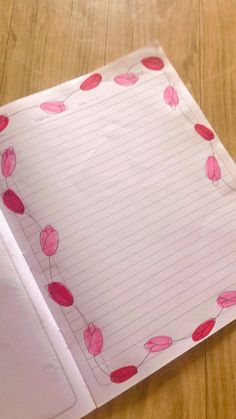 a piece of paper with pink flowers on it sitting on top of a wooden table