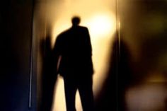 the shadow of a man standing in front of a wall with a light on it