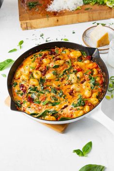 a skillet filled with pasta and spinach on top of a wooden cutting board